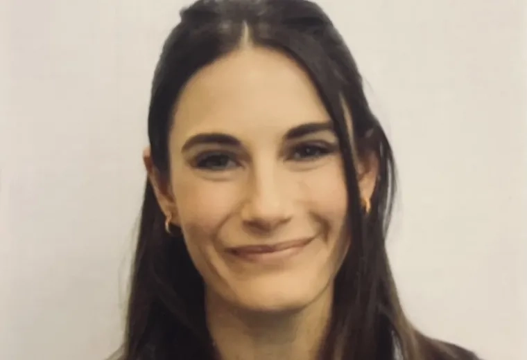 Headshot of woman with long dark hair wearing a dark blue jacket in front of a solid white background.