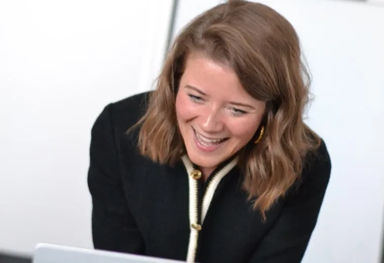 Photo of Weyland with shoulder length brown hair standing in front of a Mac laptop wearing a black top