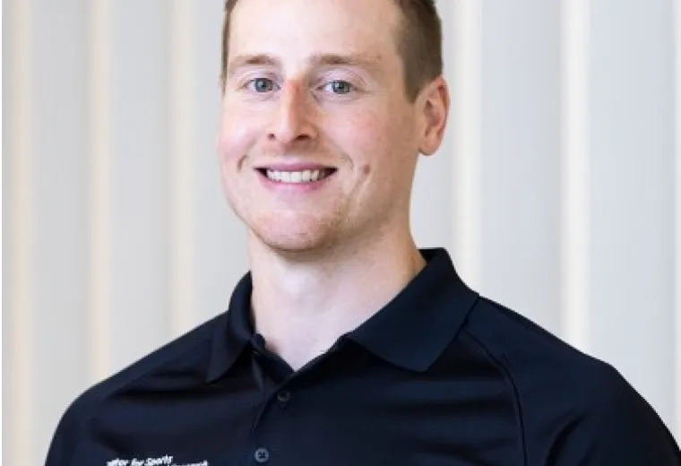 Photo of man with short hair wearing a black collared shirt in front of a white background