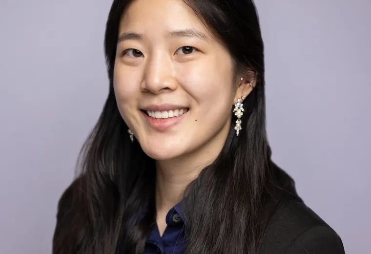 Headshot of woman with long black hair wearing a blue button-down shirt, a black jacket, and earings