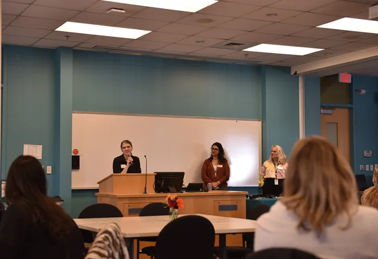 A woman speaks at a podium while two others look on