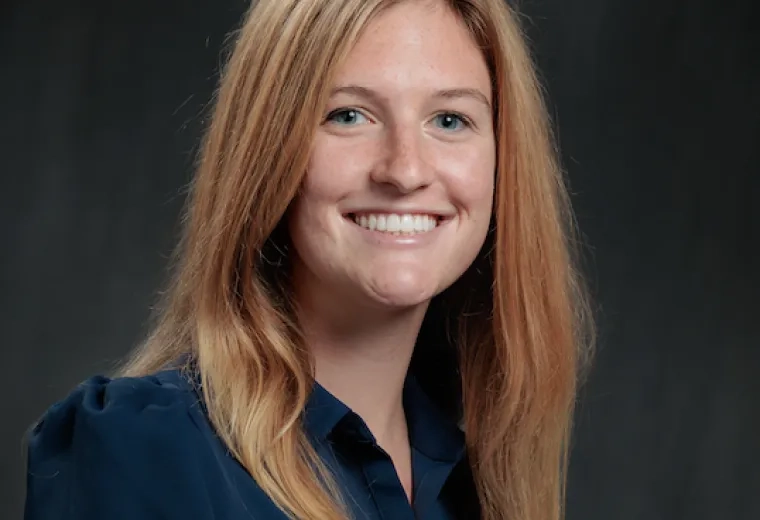 Woman with long blonde hair wearing a blue collared shirt in front of a black background