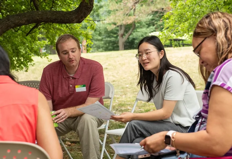 People sitting in chairs in a circle holding pieces of paper and talking to each other