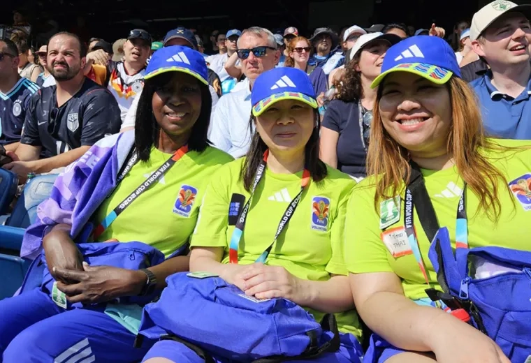 Three women sit in a stadium watching a World Cup game