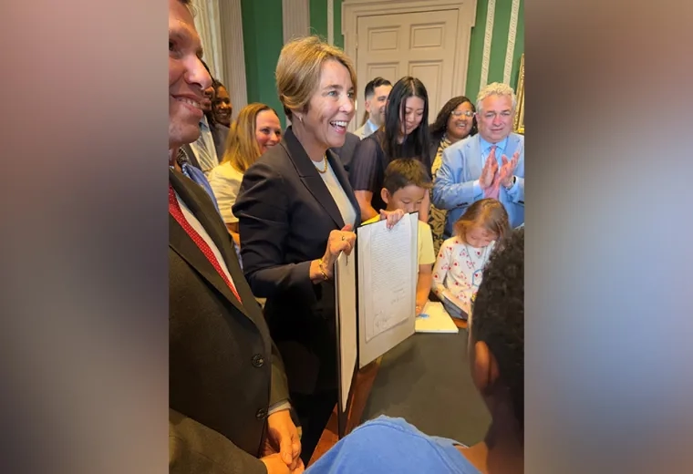 Governor Healey stands with a folder facing outwards with people gathered behind her
