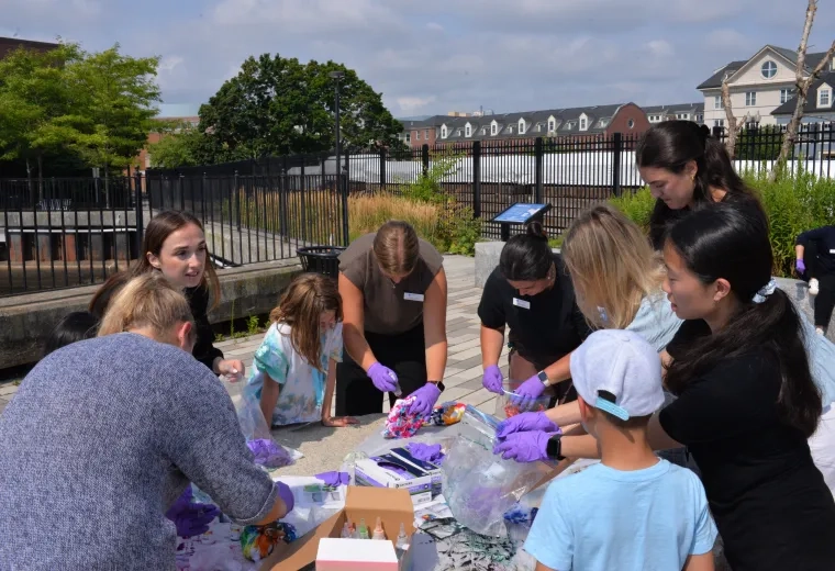 Kids and adult wear purple gloves and stand around a table dying shirts