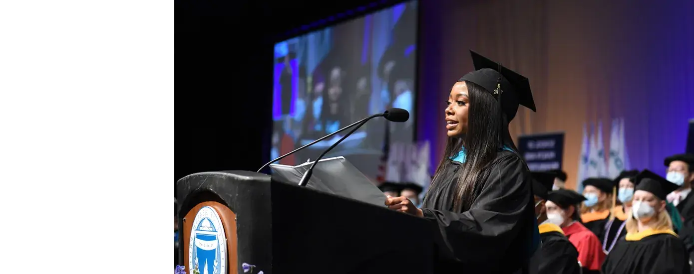 ashley stands at a podium at graduation in her cap and gown