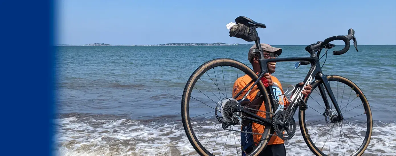 Obel-Omia holds his bike during the celebratory "wheel dip" in Revere, Massachusetts, marking the completion of the cross-country bike journey.