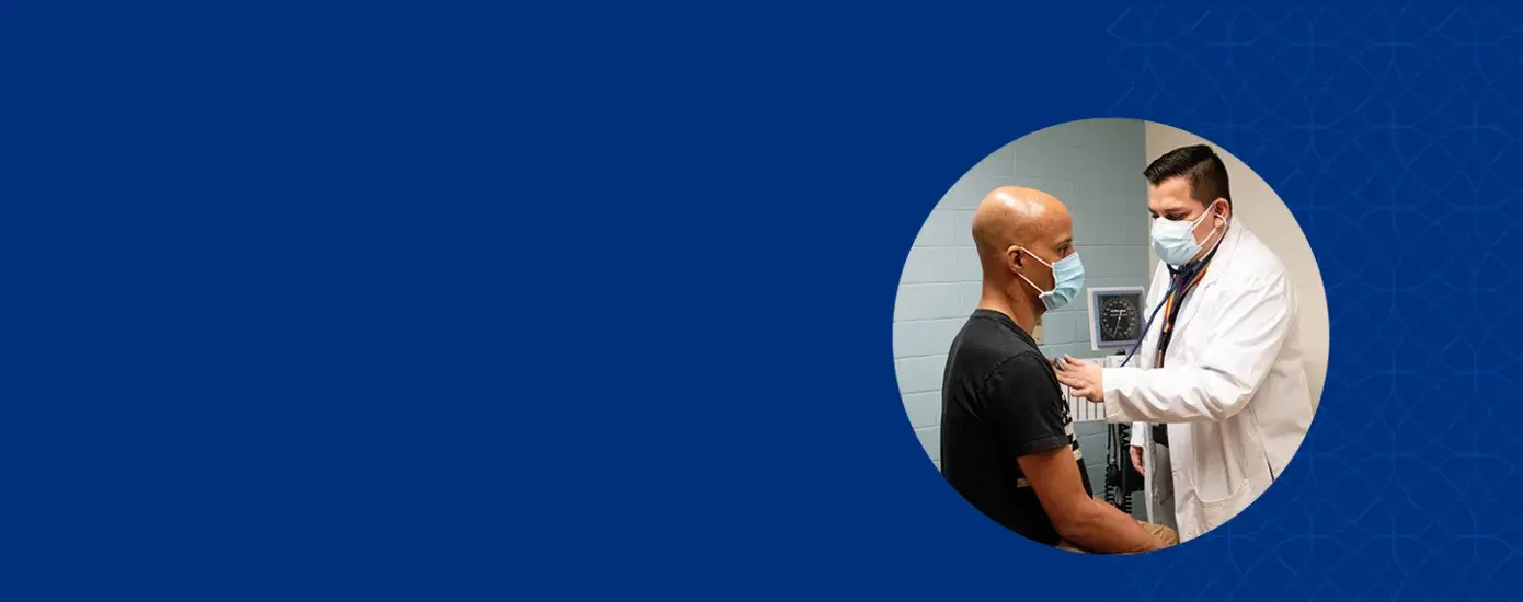 man in surgical mask listens to the heart of another man with a stethoscope