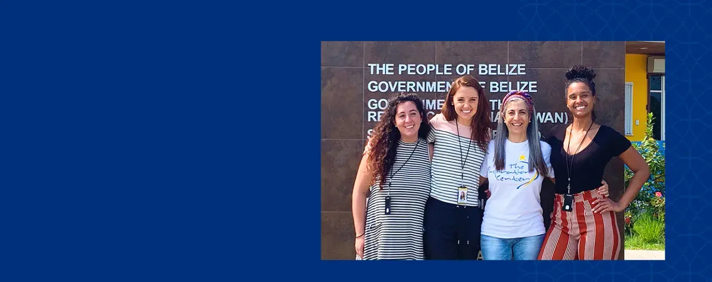 four women stand in front of a people of belize sign