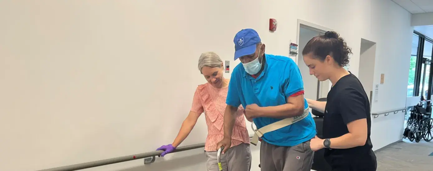 Man walks with cane and two physical therapists