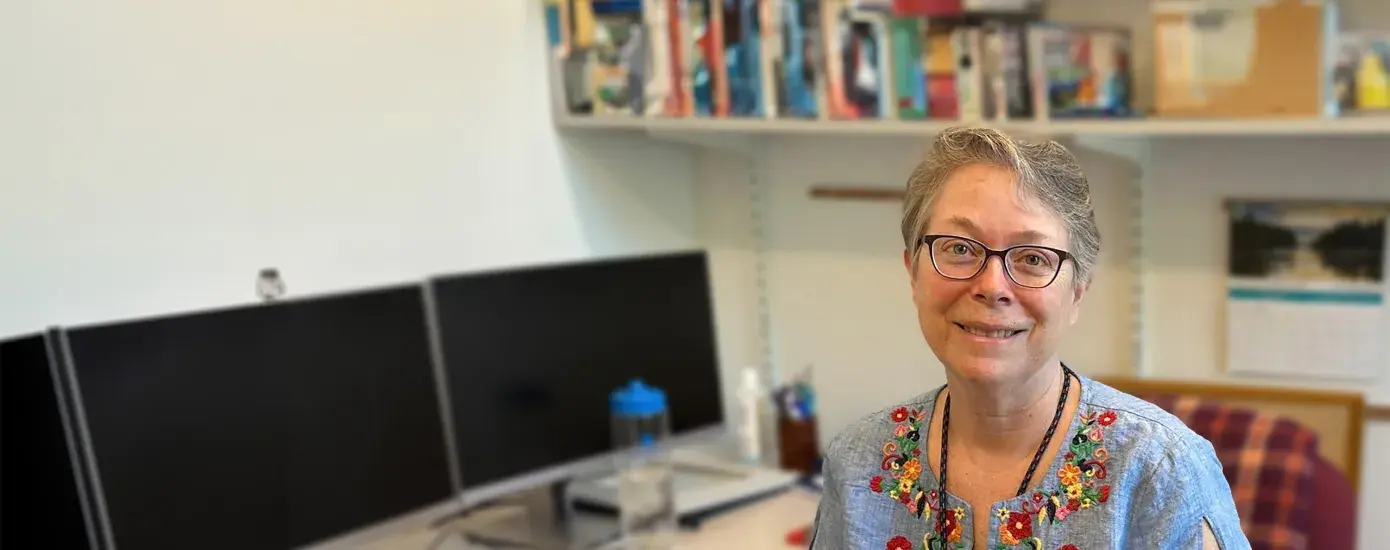 antonia has a brightly flower patterned blouse on and sits in an office chair
