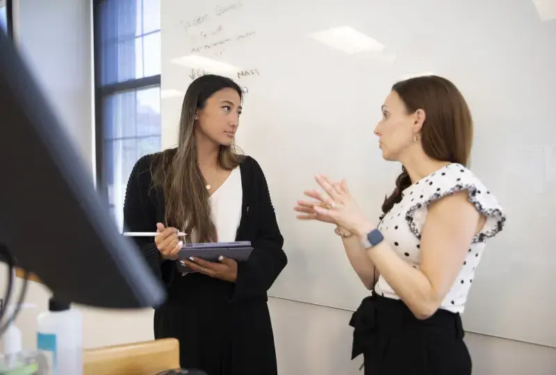 Professor gestures to a student in front of a white board