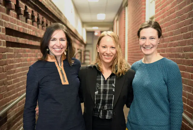 Cognitive Neuroscience Group co-chairs Sofia Vallila Rohter, Yael Arbel, and Lauryn Zipse stand in a brick hallway arm and arm