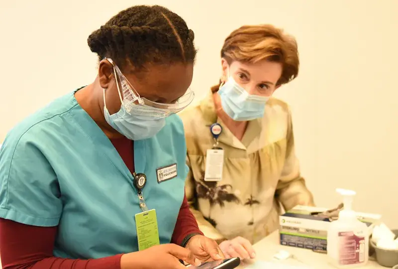 Photo of woman talking with student in scrubs, both wear masks