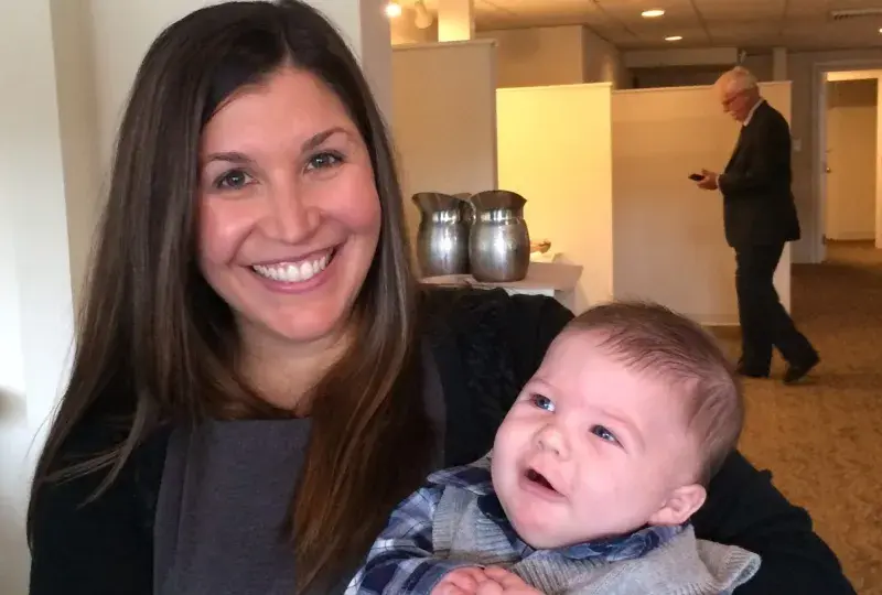 rebecca holds a baby in a sweater vest with a cute puzzled look on his face