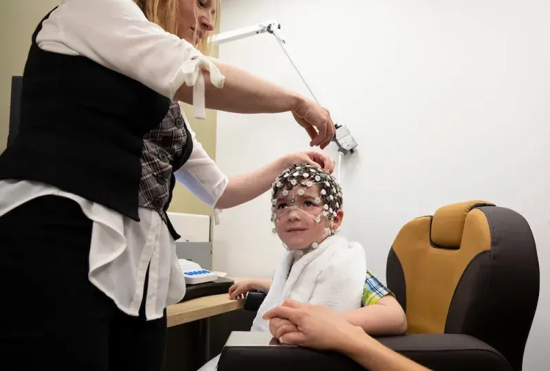 yael places a cap made of tiny white circles on a little boy's head