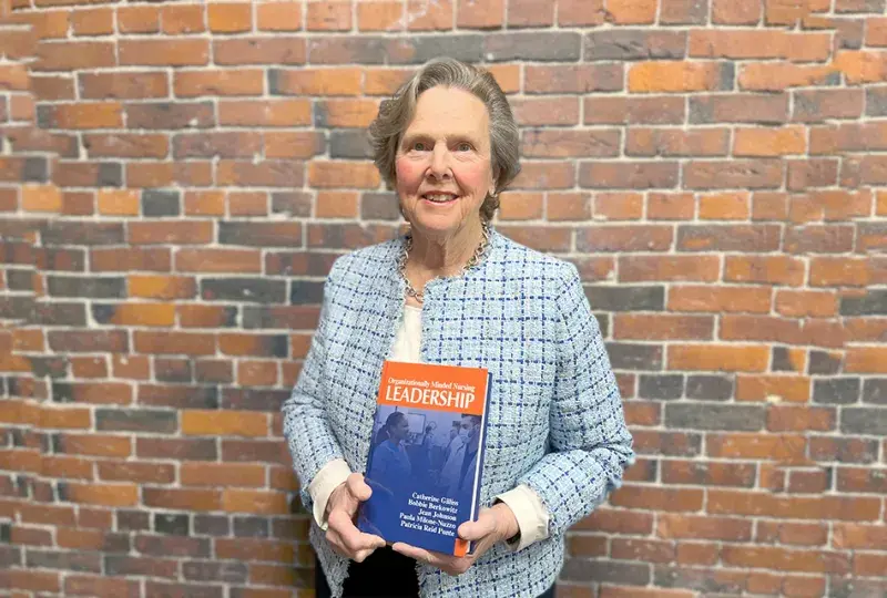 paula stands in front of a brick wall with her book
