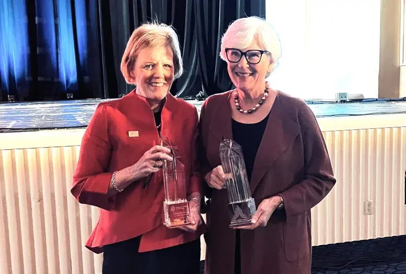 Two women smiling while holding trophies