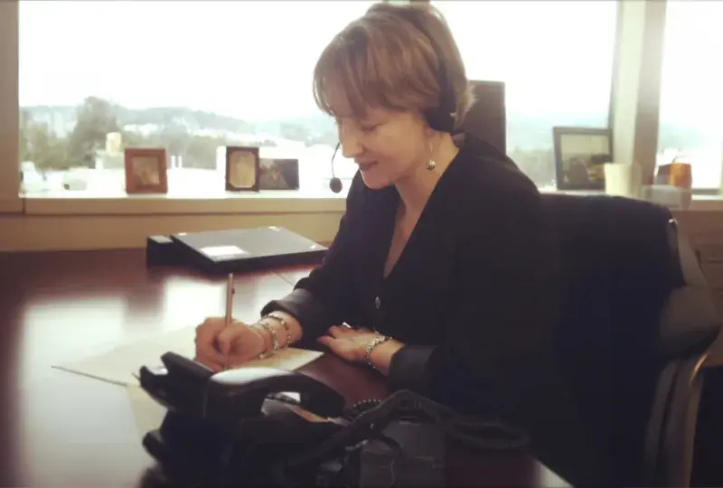 kathy sits at a desk with a headset on and takes notes on a sheet of paper