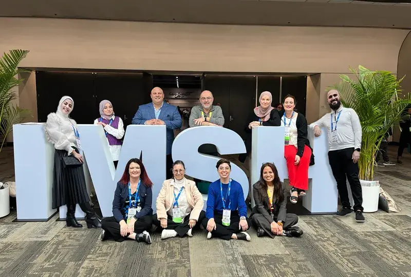 group of people stand in front of and within large letters spelling IMSH