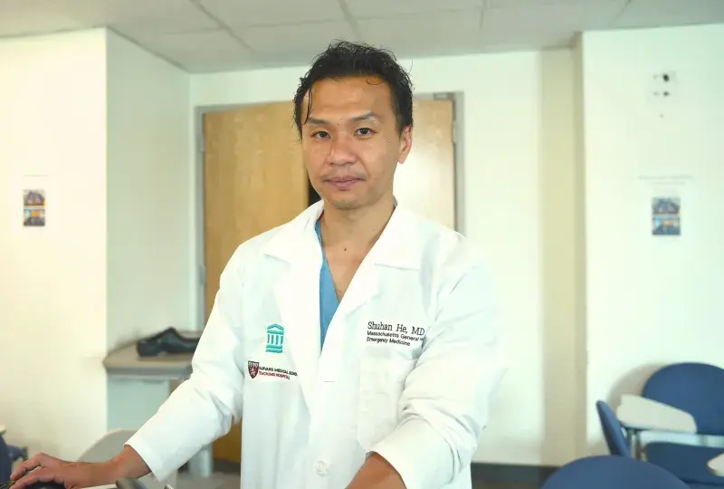 shuhan stands at a computer in a clinical office and wears a white coat 