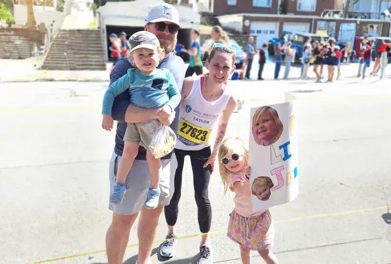 women in tank top with race bib attached smiles with man and two children in the street