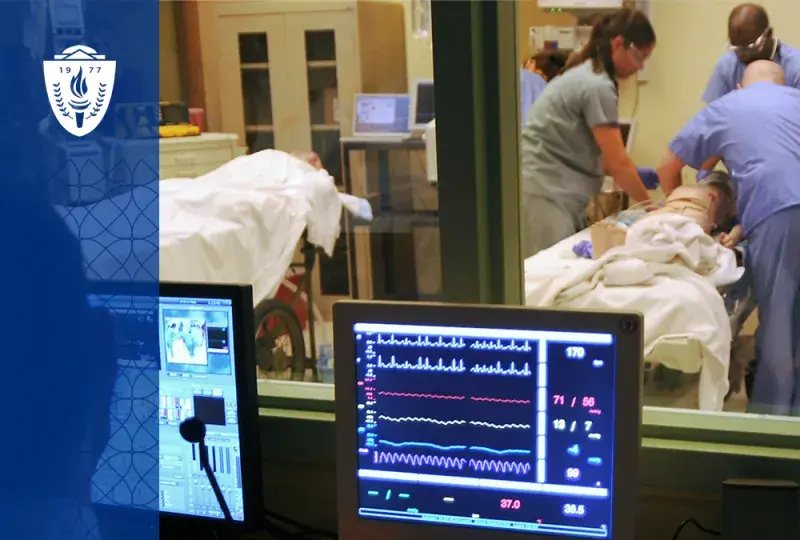 a computer screen with lines monitoring vitals like heartbeats is in front of a window where people in scrubs are working on a manikin in a hospital bed