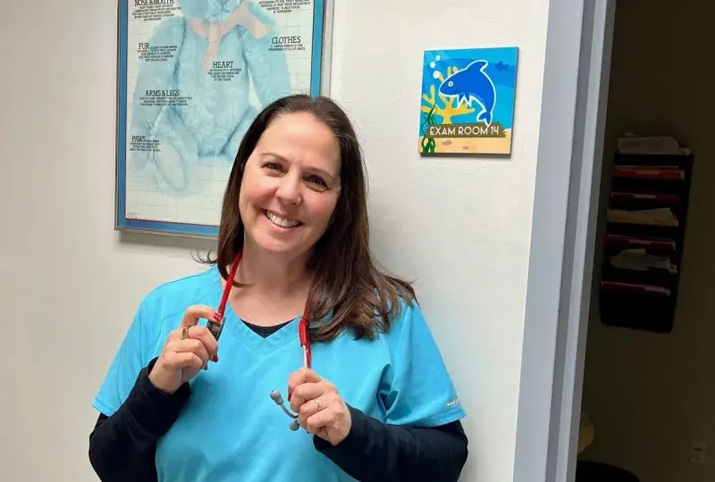 woman in blue scrubs with stethoscope around neck and big smile