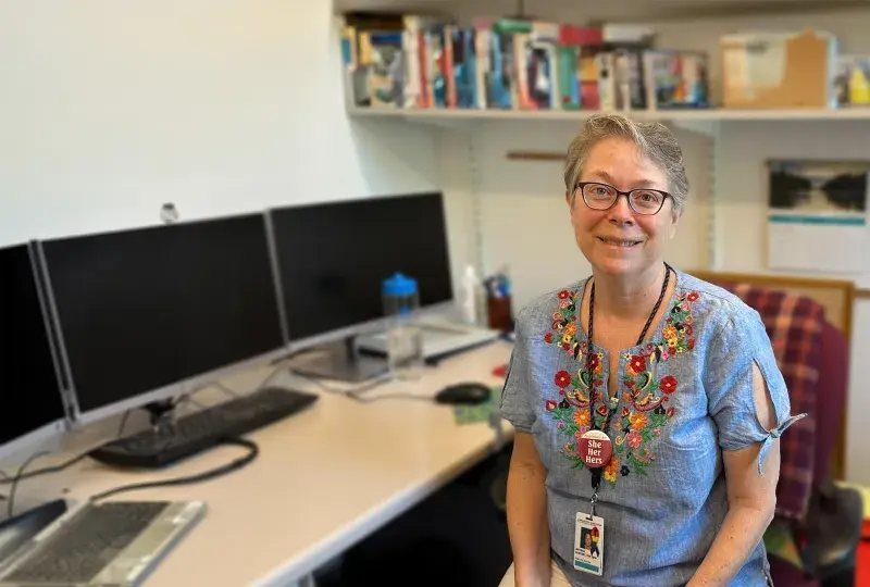 antonia has a brightly flower patterned blouse on and sits in an office chair