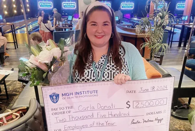 A woman poses holding flowers and a large check