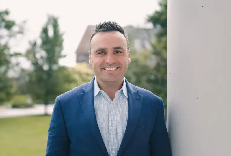 Kevin Finn is wearing a blue suit jacket and light blue shirt. He has short brown hair.