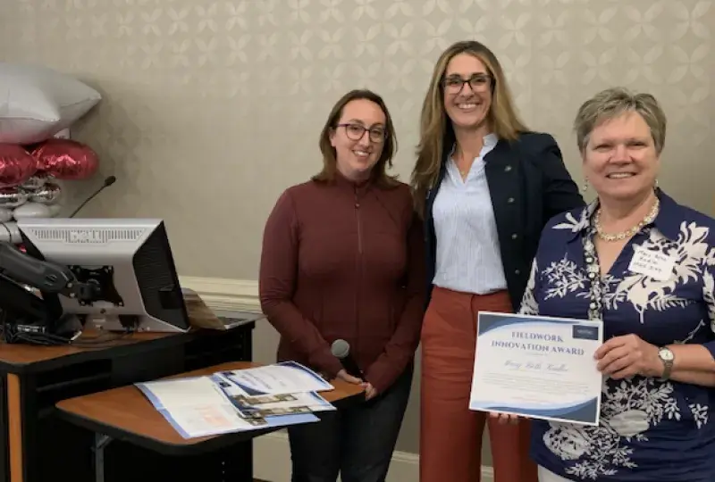 Three women smile while holding a certificate.