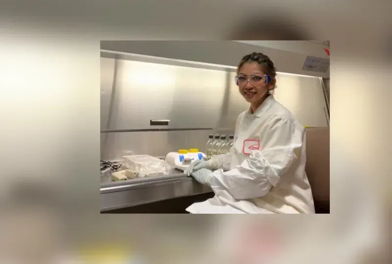 junny sits in a lab with a lab coat and lab glasses on