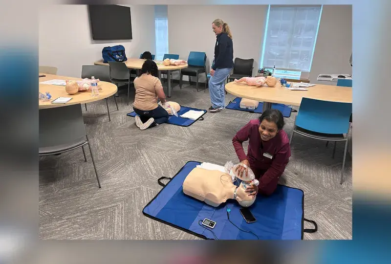 woman kneels in front of a manikin torso on the floor
