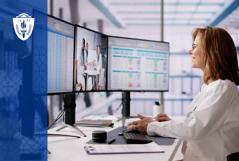 a woman in a white lab coat looks at data on three computer screens