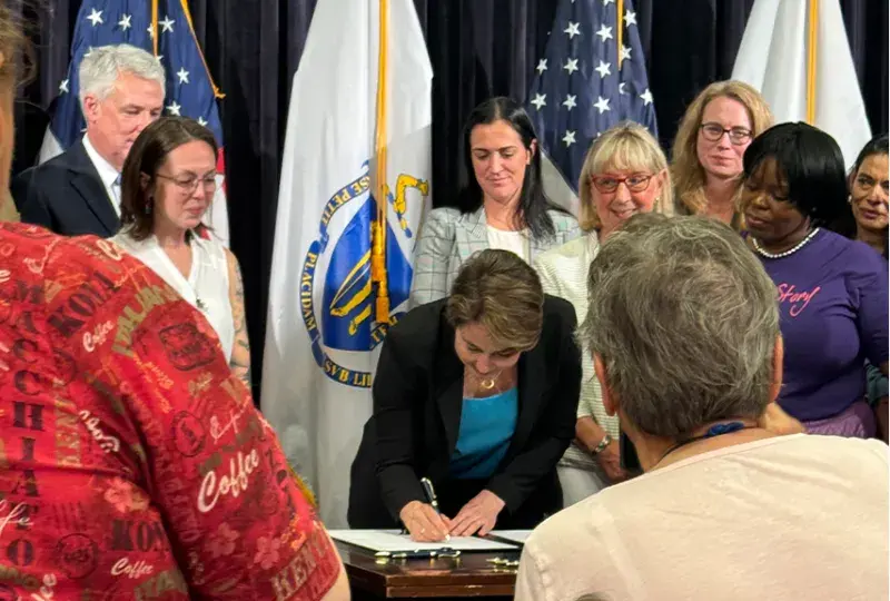 woman signs paper at desk with people all around
