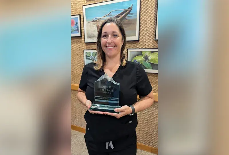 A woman holds an acrylic award with the words NBCOT Impact Award engraved on it