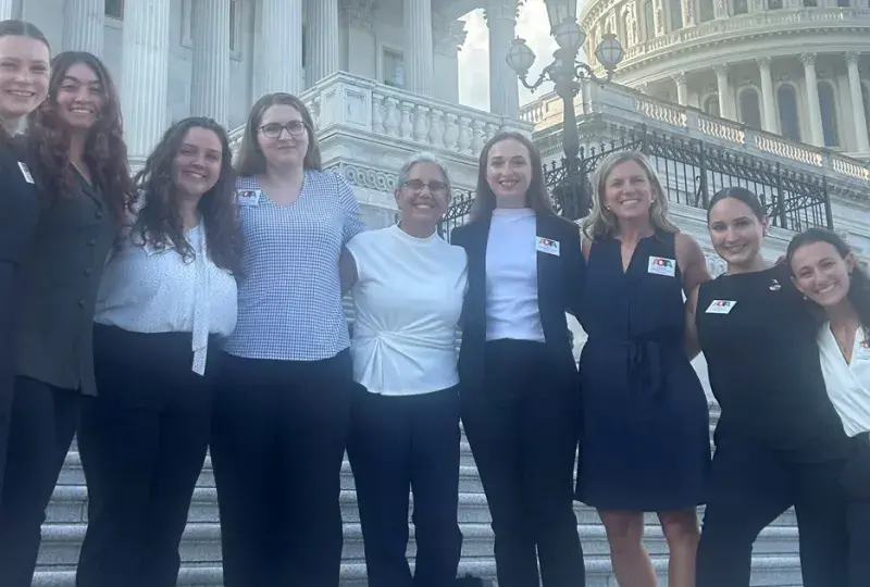 Nine people stand on steps with the US Capitol in the background