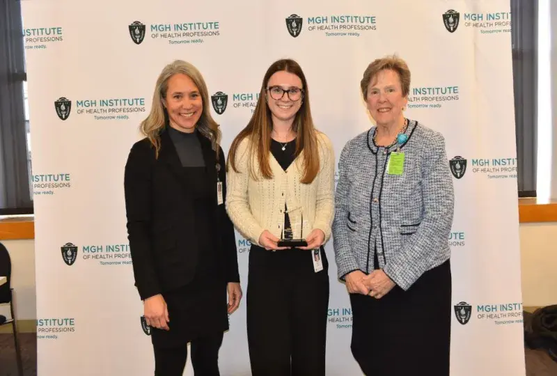 Three people stand in front of a background holding an award