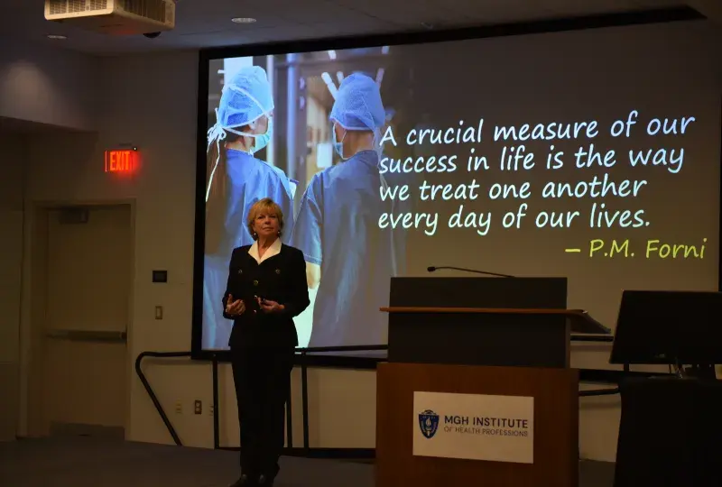A woman stands in front of a screen with a quote
