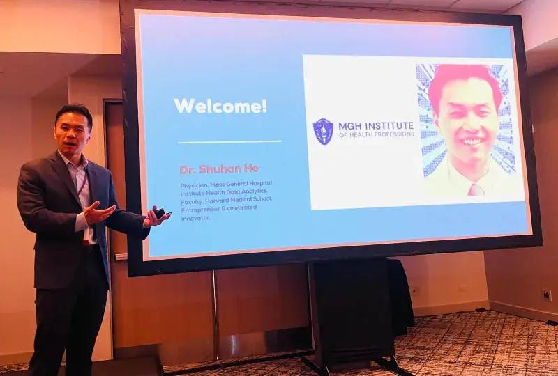 A man stands in front of a screen with his photo and the word Welcome on it. 
