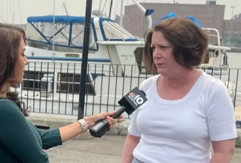 A women on the left holds a microphone with a camera behind her while another women speaks into the microphone