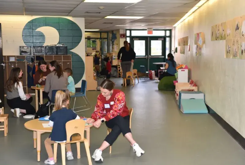 A woman sits at a small table with a child while people in the background do the same