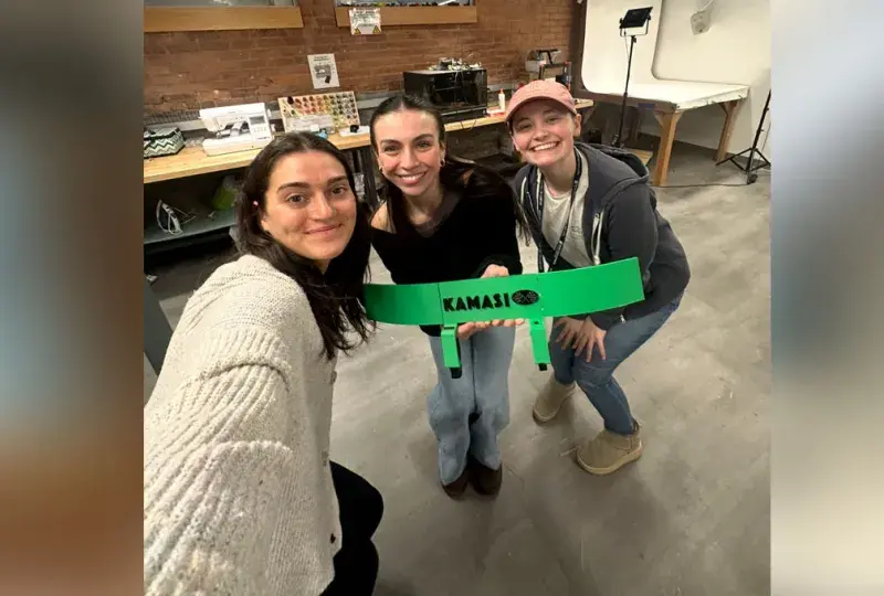 Three women pose holding up a green device
