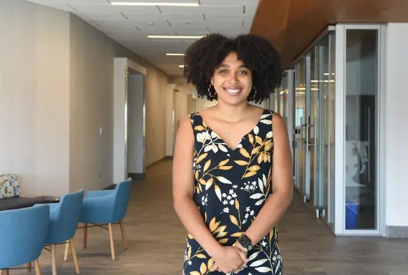 A woman stands with chairs to her right and glass rooms to her left