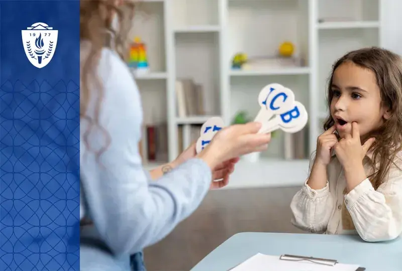 Young girl sitting at desk looking at a teacher holding sticks with alphabet letters on them