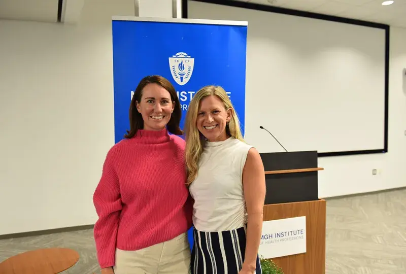 Two women stand in front of a blue back drop