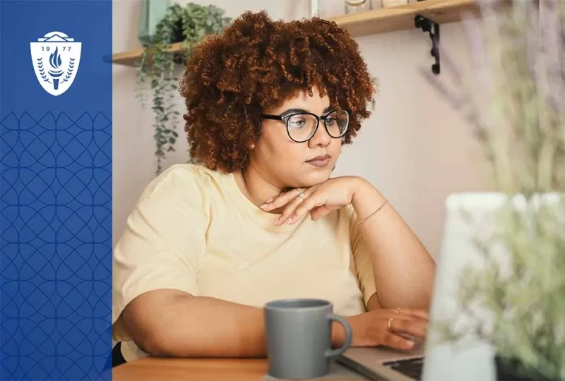 Woman wearing a yellow shirt sitting at a desk working on a laptop next to a coffee mug