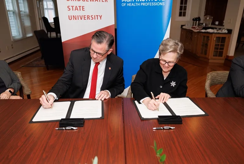 Two people sit at a table signing paper